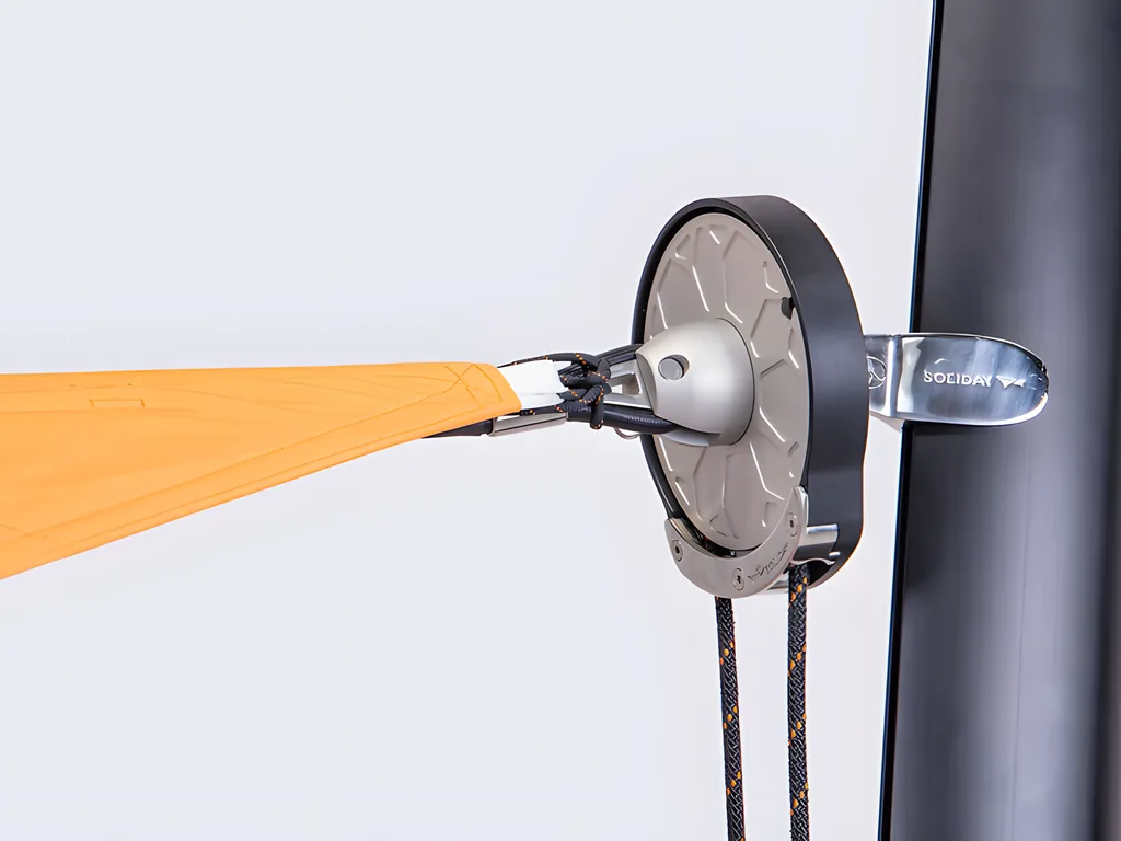 A black pulley wheel on a pole, holding the orange edge of a sail