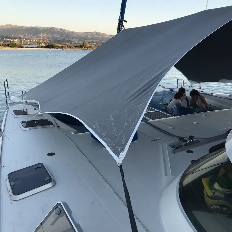 White shade sail over the bow of a catamaran on open water
