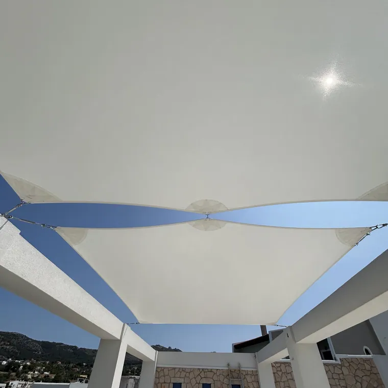White sails seen from below against the sun, over a stone terrace