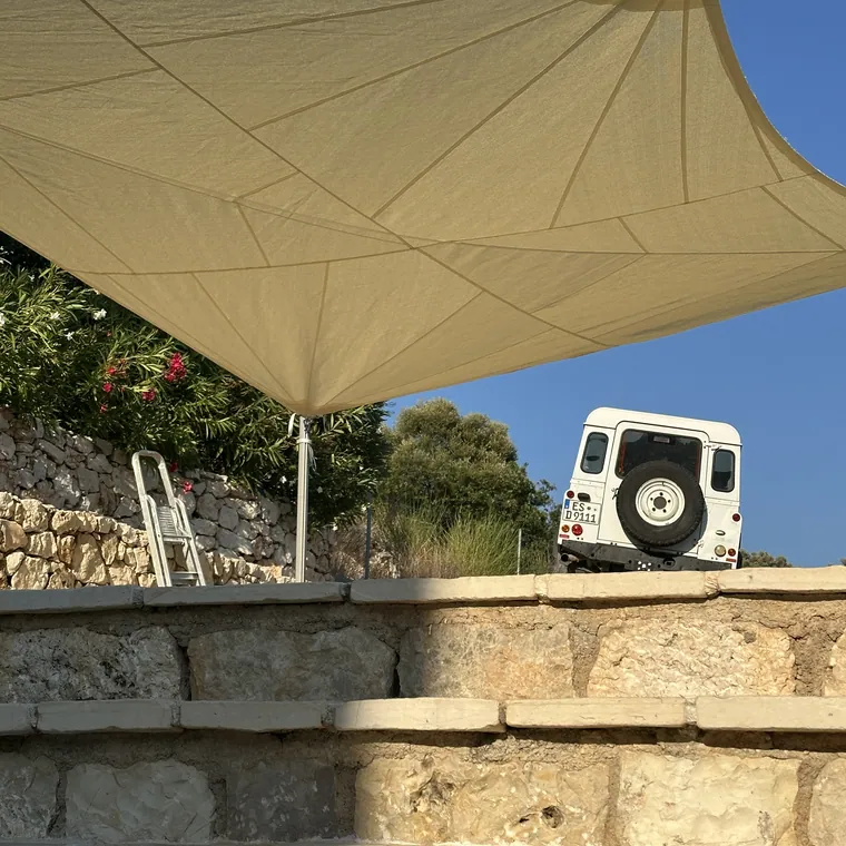 Sand sail on stainless poles over a garden and a stone wall