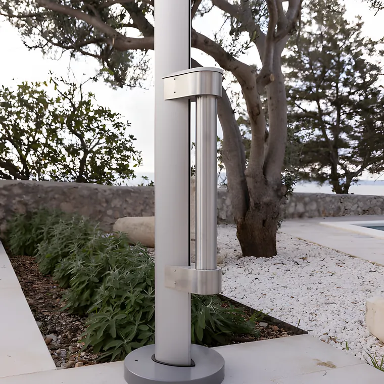 A slim aluminium pole standing in a gravel bed beside an olive tree
