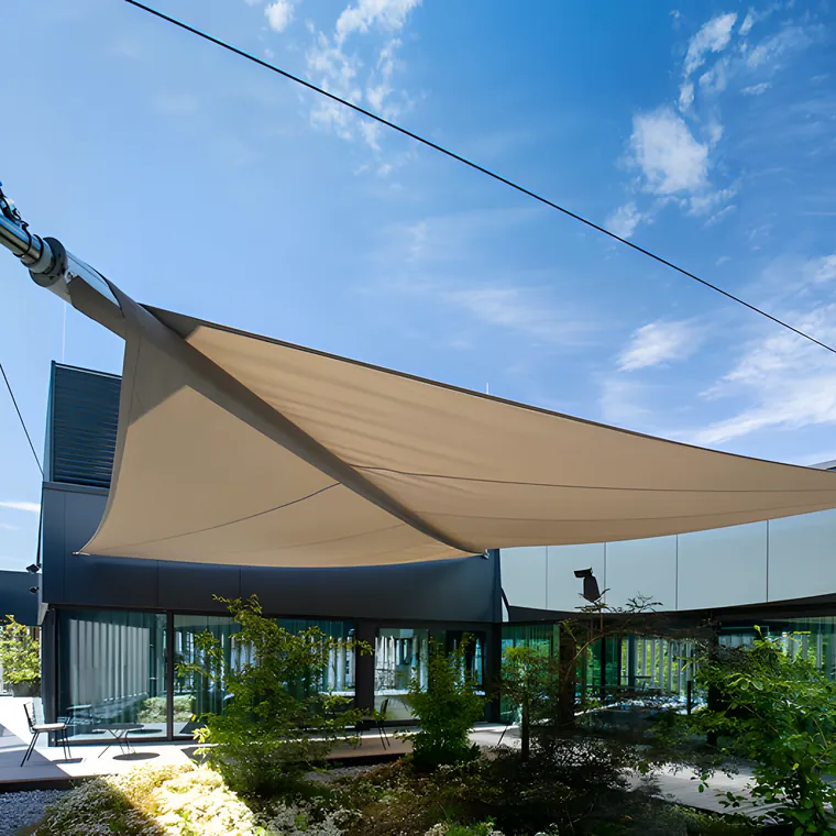 A large cream sail tensioned on cables above a glass building