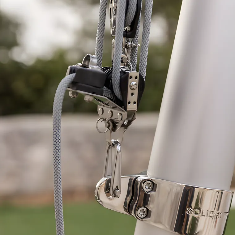 A pulley block and a stainless clamp band fixed to a pole above a lawn