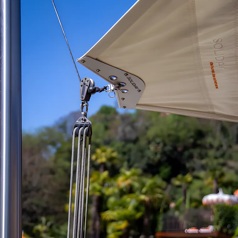 The corner of a cream sail on a stainless plate, the wire and the pole below it
