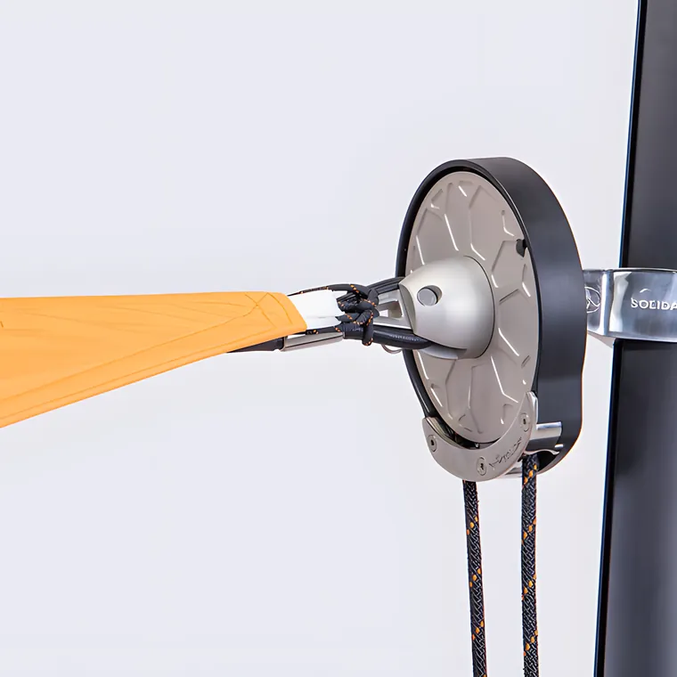 A black pulley wheel on a pole, holding the orange edge of a sail