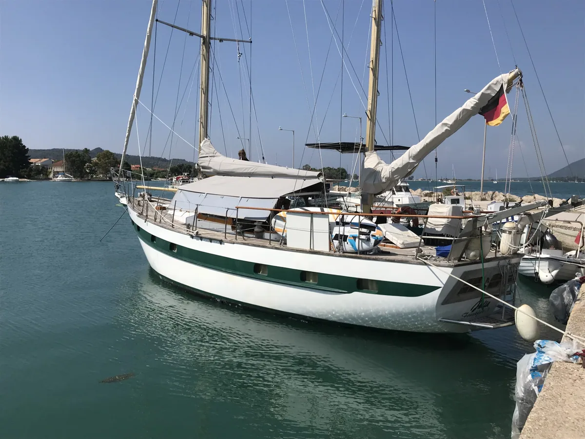Classic green and white ketch on its mooring with the sail covers on