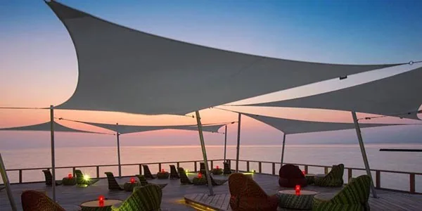 Dark shade sails over a terrace bar at sunset above the sea