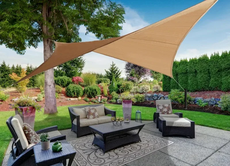 Tan triangular sail stretched over a garden lounge between trees