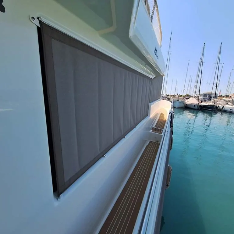 Beige shade fitted over a saloon window, the marina visible past it